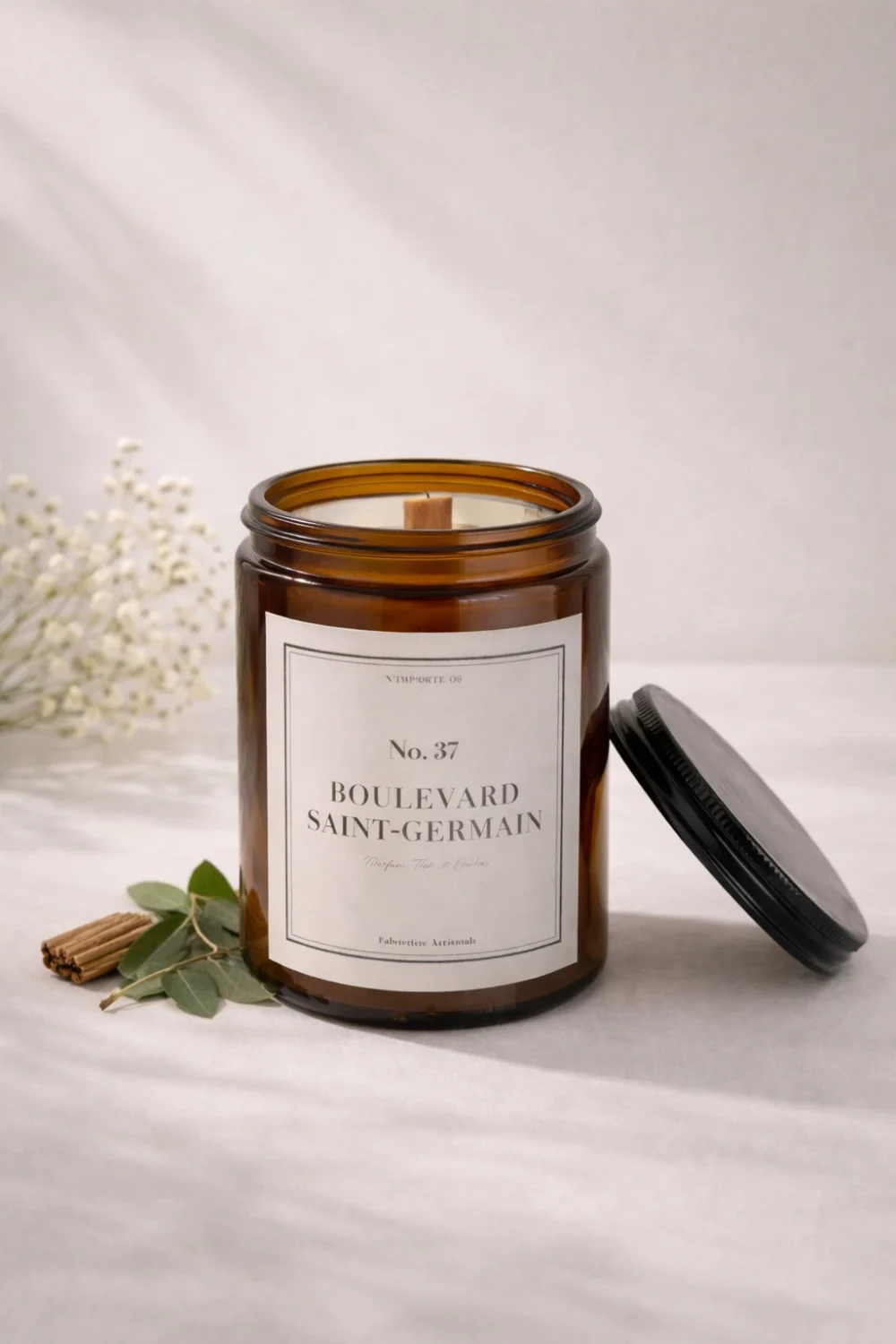 Bougie parfumée artisanale 37 Boulevard Saint-Germain, étiquette blanche sobre, posée sur un vieux livre à la reliure en cuir usée, ambiance salon de lecture ancien.