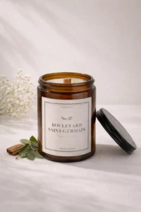 Bougie parfumée artisanale 37 Boulevard Saint-Germain, étiquette blanche sobre, posée sur un vieux livre à la reliure en cuir usée, ambiance salon de lecture ancien.