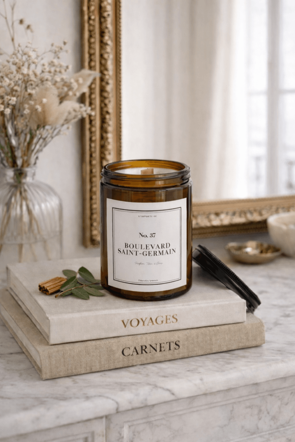 Bougie parfumée artisanale 37 Boulevard Saint-Germain, étiquette blanche sobre, posée sur un vieux livre à la reliure en cuir usée, ambiance salon de lecture ancien.