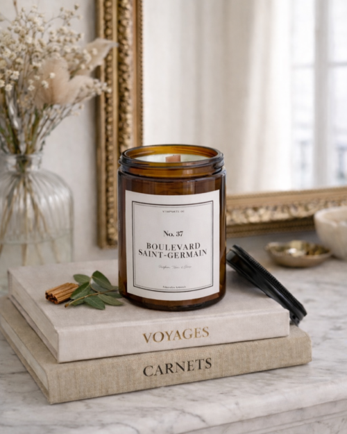Bougie parfumée artisanale 37 Boulevard Saint-Germain, étiquette blanche sobre, posée sur un vieux livre à la reliure en cuir usée, ambiance salon de lecture ancien.