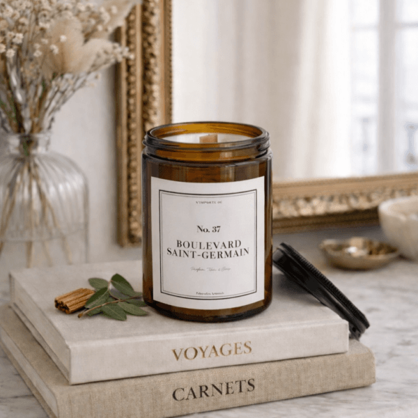 Bougie parfumée artisanale 37 Boulevard Saint-Germain, étiquette blanche sobre, posée sur un vieux livre à la reliure en cuir usée, ambiance salon de lecture ancien.