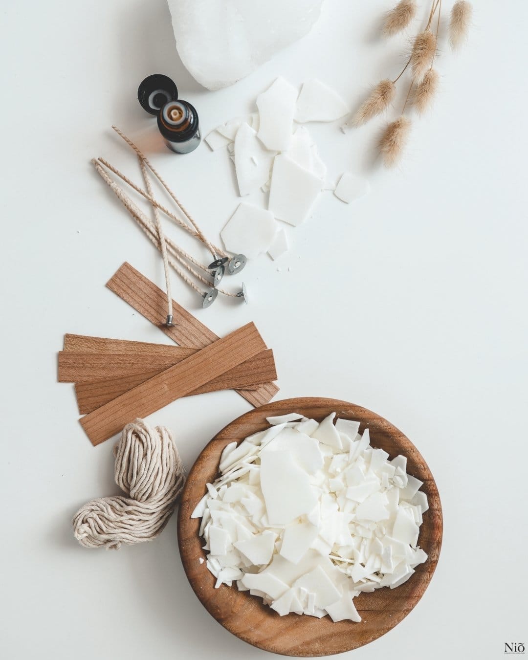 image HERO savoir faire et matière - Niõ Image représente un récipient avec la cire de soja, les mèches en coton et en bois, un brin de la lavande séchée, une fiole de fragrance, représentant le savoir-faire et matières de Niõ